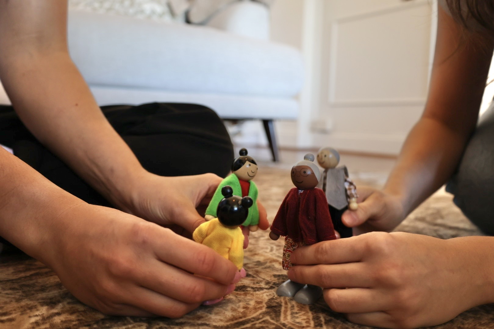 Tamsyn and a child playing with wooden dolls together on a patterned rug at home